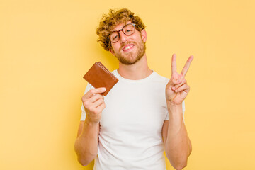 Young caucasian man holding a wallet isolated on yellow background joyful and carefree showing a...