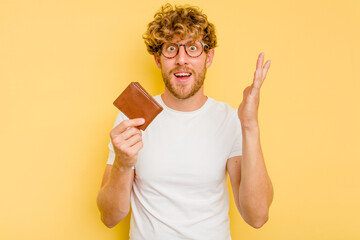 Young caucasian man holding a wallet isolated on yellow background receiving a pleasant surprise,...