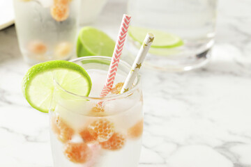 Glass and jug with fresh water and lime on marble table. Space for text. Flavored water. Summer drinks. Raspberry, mint and lime.