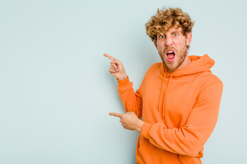 Young caucasian man isolated on blue background pointing with forefingers to a copy space, expressing excitement and desire.