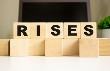 The word RISES is written on wooden cubes lying on the office table in front of a laptop.
