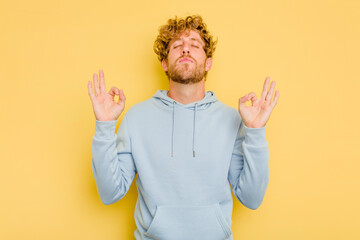 Young caucasian man isolated on yellow background relaxes after hard working day, she is performing...