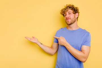 Young caucasian man isolated on yellow background excited holding a copy space on palm.