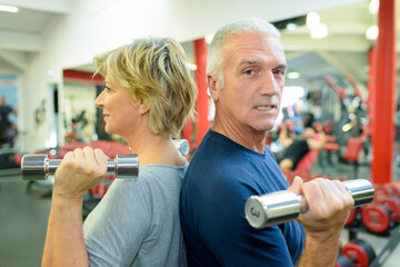 senior couple in gym working out with weights