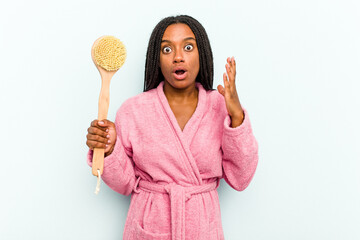 Young African American woman holding a bathtub brush isolated on blue background surprised and shocked.