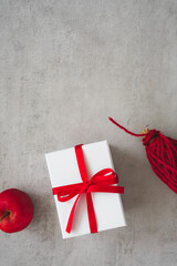 Eine weiße Geschenk Box mit roter Schleife, ein Apfel und eine Schnur Spule auf einem grauen Tisch.