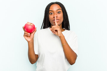 Young African American woman holding an apple isolated on blue background keeping a secret or asking for silence.