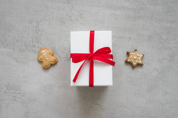 Eine weiße Geschenk Box mit roter Schleife und Lebkuchen Kekse auf einem grauen Tisch. Draufsicht.