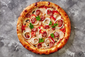 Pizza with hunting sausages, smoked chicken, mushrooms, bell peppers and onion on gray stone surface