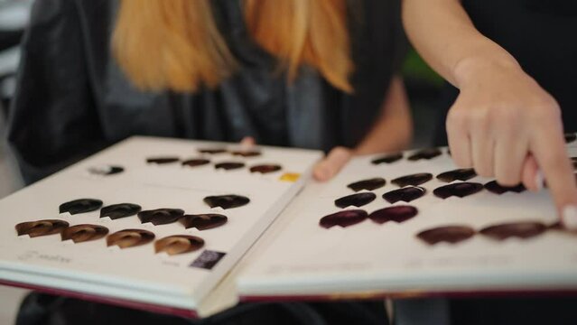 Woman hairdressers presents samples of paint for hair with customer open a book thick cardboard pages in a beauty salon