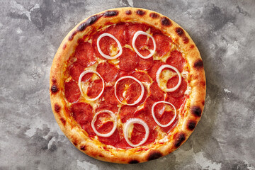 Top view of pepperoni pizza with tomato sauce, mozzarella cheese and onion rings on gray stone