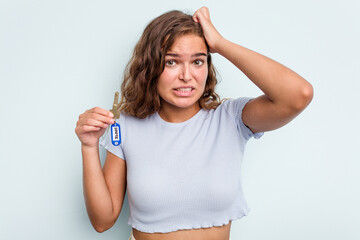 Young caucasian woman holding home keys isolated on blue background being shocked, she has...