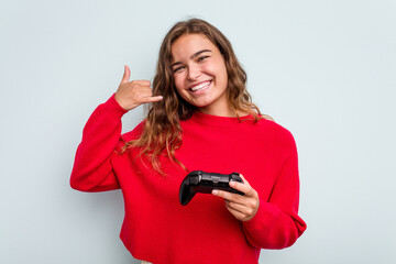 Young caucasian gamer woman holding a game controller isolated on blue background showing a mobile...