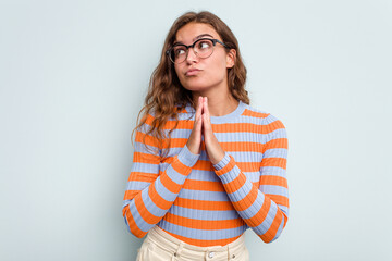 Young caucasian woman isolated on blue background praying, showing devotion, religious person looking for divine inspiration.