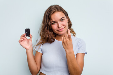 Fototapeta premium Young caucasian woman holding car keys isolated on blue background pointing with finger at you as if inviting come closer.