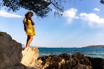 beautiful long-haired girl in a yellow dress enjoys the sunset on a paradise beach in croatia, peljesac peninsula and its paradise bays