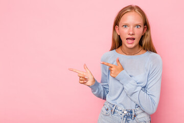 Caucasian teen girl isolated on pink background pointing with forefingers to a copy space,...