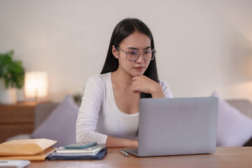 Beautiful Asian woman sitting intently working on a laptop computer at home.