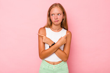 Fototapeta premium Caucasian teen girl isolated on pink background points sideways, is trying to choose between two options.