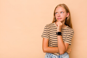 Caucasian teen girl isolated on beige background looking sideways with doubtful and skeptical expression.