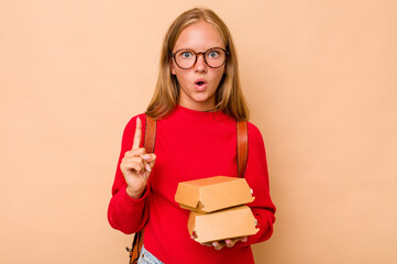 Little caucasian student girl holding burgers isolated on beige background having some great idea, concept of creativity.