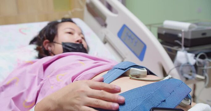 Pregnant woman lying in a hospital bed, fetal monitor strapped to her belly, Pregnant woman in labor with fetal heart rate monitor in hospital, healthcare during pregnancy