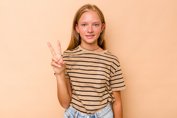 Caucasian teen girl isolated on beige background showing victory sign and smiling broadly.