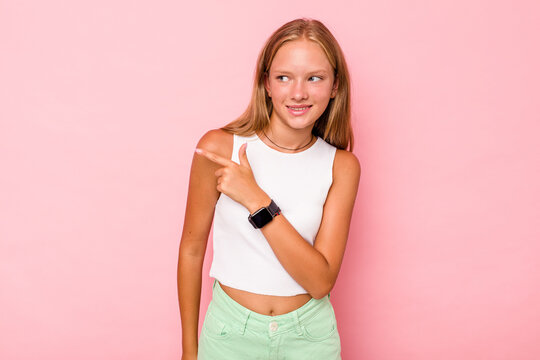 Caucasian teen girl isolated on pink background looks aside smiling, cheerful and pleasant.