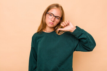 Caucasian teen girl isolated on beige background showing a dislike gesture, thumbs down....