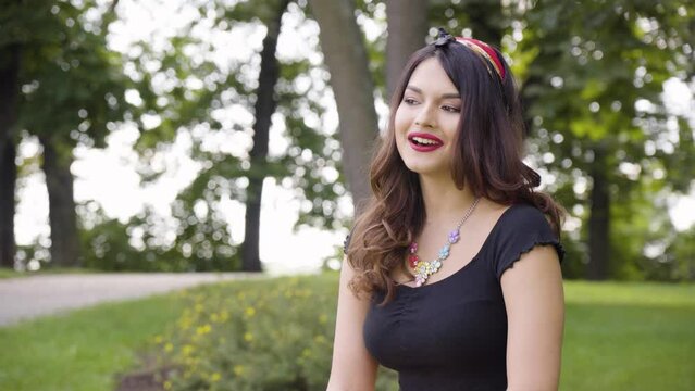 A young beautiful Caucasian woman talks to the camera with a smile in a park on a sunny day