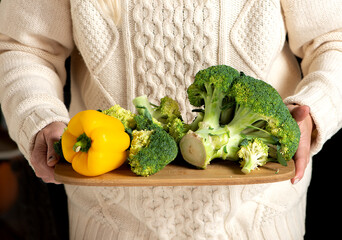 Close-up of woman hands holding cutting board with fresh  vegetables- organic broccoli and yellow...