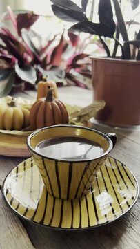 Cozy Home Fall Decorations with Cup of Coffee, Pumpkin Candles and Houseplants on Wooden Table. Autumn weekend concept