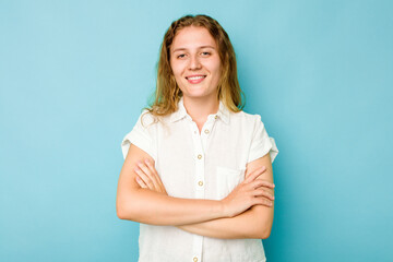 Young caucasian woman isolated on blue background who feels confident, crossing arms with determination.