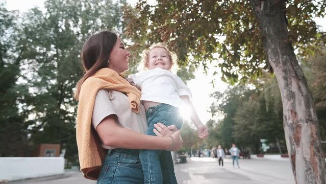 Loving mother walks with her cute daughter in the park. Mom holds her daughter in her arms, the girl grimaces. Contour light of the sun. loving family
