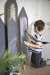 Cute baby boy drawing on black chalkboard colorful chalks indoor at childish playroom kindergarten
