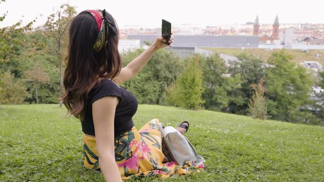 A young beautiful Caucasian woman takes selfies with a smartphone in a park on a sunny day