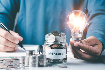 Young man holding a light bulb,coin in a glass jar,Finance and investment concepts, growth from profits and dividends,Investing in the stock market and trading cryptocurrencies,future income planning