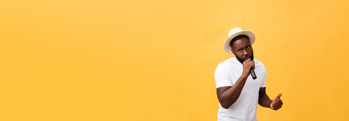 Fototapeta na wymiar young handsome african american boy singing emotional with microphone isolated on yellow background, in motion gesturing
