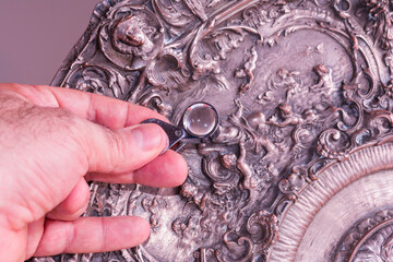 Art restorer holds magnifying glass to examine mid-19th century French art piece.
