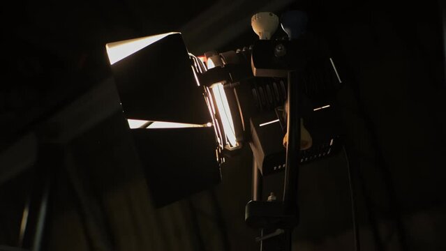 Halogen source of constant lighting equipment. Lightweight fresnel spotlight searchlight is on set during shooting of film. Lamphead. Dark stage, scene. Movie cinema production. Gafer's work on-set
