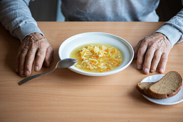 View from above of a soup plate, bread and the untidy hands of an old man
