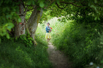 Obraz premium Woman in yellow dress gathering poppy and wildflowers, walking in summer meadow. Atmospheric authentic moment. Rural slow life in countryside