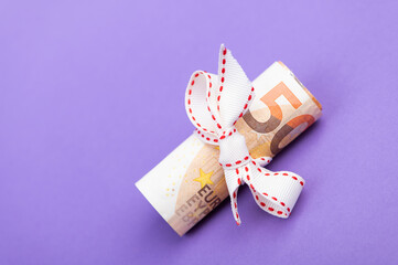fifty euro banknote money roll tied with a white gift ribbon isolated on a purple background