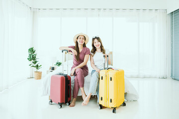 Portrait of Two travel woman smile happily with suitcase and passport in bed. Pretty girls planning vacation trips in the summer within the interior bedroom at home. 