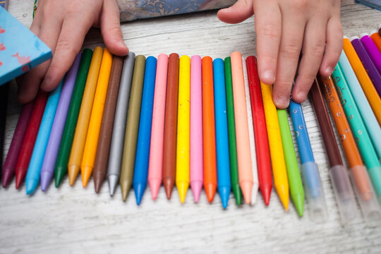 manos de niña ordenando ceras de colores en una mesa
