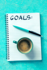 Goal setting. A notebook with the handwritten word Goals, with a cup of coffee and a pen, overhead flat lay shot on a vibrant blue background. The concept of writing a list or a plan