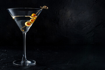 Martini, a glass with spicy olives on a toothpick, on a black background. Alcoholic drink with copy space