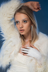 pierced young woman with winter makeup posing in white jacket with feathers on dark blue.