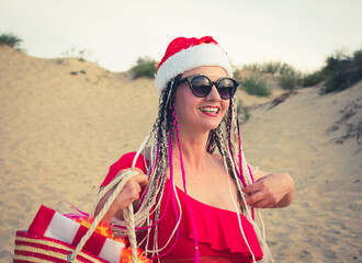 Happy middle aged attractive brunette woman in red swimsuit and Santa hat having fun on the coast. Christmas holiday vacation and travel concept.