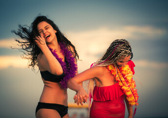 Mother and daughter teenager fooling around walking together on beach holding hands, woman and girl in swimsuits enjoying the sea and sunset. Vacation, family, summertime, copy space